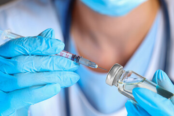Doctor inserting syringe into glass vial with medication, closeup