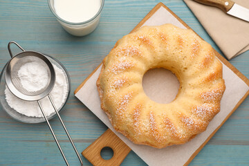 Delicious sponge cake with powdered sugar and glass of milk on light blue wooden table, flat lay