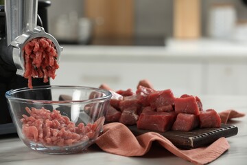Electric meat grinder with beef mince on white table against blurred background, closeup. Space for...