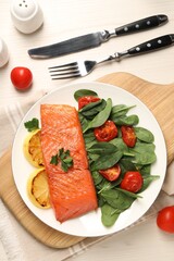 Tasty grilled salmon with basil, tomatoes and lemon on white wooden table, flat lay