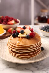 Delicious pancakes with fresh berries, butter and honey on white marble table, closeup