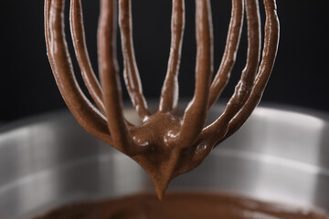 Chocolate cream flowing from whisk into bowl on black background, closeup