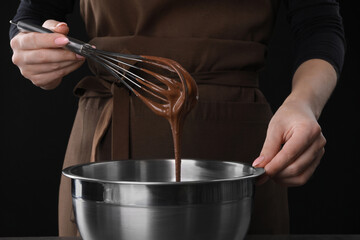 Woman with whisk mixing chocolate cream on black background, closeup