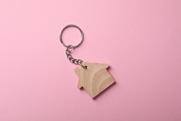 Wooden keychain in shape of house on pink background, top view