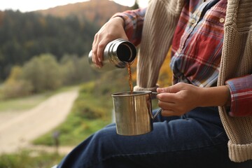 Woman pouring hot drink from thermos into metallic mug outdoors, closeup. Space for text