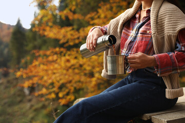 Woman pouring hot drink from thermos into metallic mug outdoors, closeup. Space for text