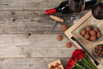 Red wine, chocolate truffles, corkscrew, roses and gift box on wooden table, flat lay. Space for text