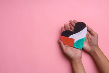 Hand holding heart shape paper symbolizing Palestinian flag on pink background