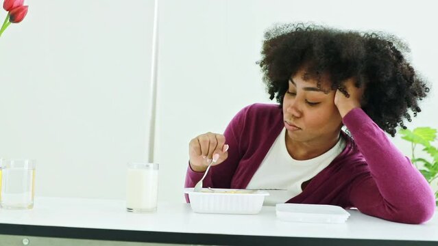 African American teenage girl tired of eating unsatisfying, unhealthy boxed meals. Sitting and staring at bland boxed food, using a spoon to dig into the nutritious rice.