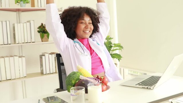 Female doctor nutritionist doing stretching exercises and lifting dumbbells in the clinic office lightly with happiness smiling at the camera, relaxing in her daily life style.