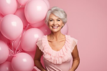 Obraz na płótnie Canvas Portrait of attractive attractive mature senior woman in pink dress against background of pink helium party balloons. Valentine’s or Birthday party