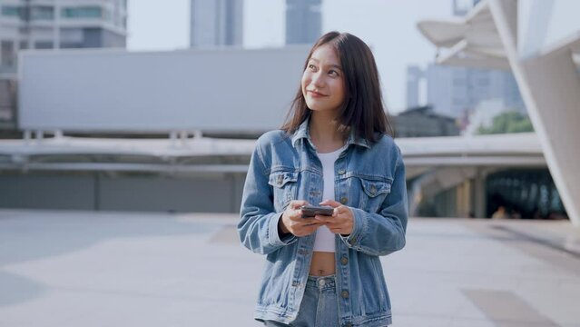 Young asian woman in jeans jacket clothes texting on smartphone walking on street in city on sunny day