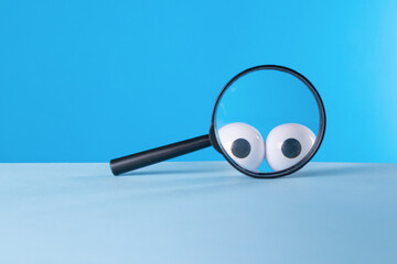 Creative image of a magnifying glass with eyes on a blue background.