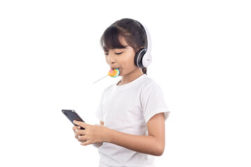 Fototapeta premium A happy Asian young girl playing music with her smartphone and wearing headphones and eating a lollipop isolated on white background with clipping path.