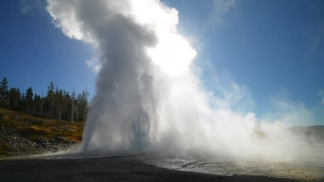Cinematic Grand Old Faithful geyser sun glare sunrise sunset eruption explosion steam Yellowstone National Park observation deck Upper Geyser Basin fall autumn beautiful blue sky slow motion zoom
