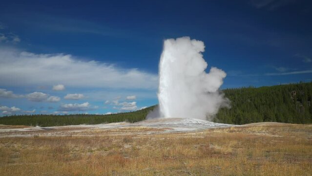 Cinematic famous Old Faithful geyser sunrise sunset eruption Yellowstone National Park observation deck viewing area Upper Geyser Basin active volcano  fall autumn beautiful blue sky slow motion pan
