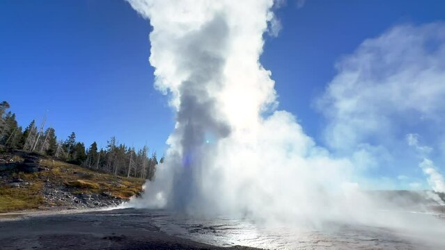 Cinematic Grand geyser Old Faithful sun glare sunrise sunset eruption explosion steam Yellowstone National Park observation deck Upper Geyser Basin fall autumn beautiful blue sky slow motion still