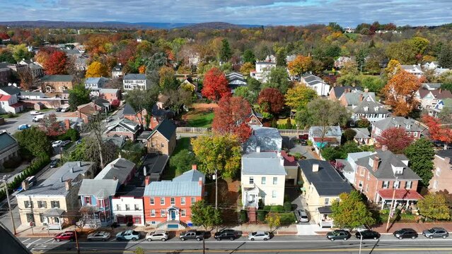 Small town America in autumn. Aerial truck shot of houses and homes lining street in suburban neighborhood. Autumnal trees with colorful fall foliage.