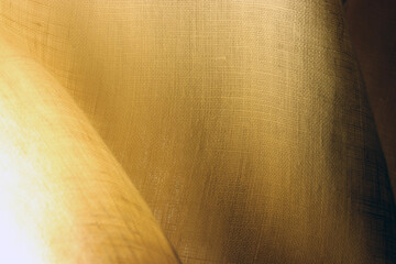 Dark pale golden texture of fine linen fabric with rich drape. Back light effect photography.