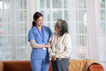 Obraz premium Happy asian female doctor helping elderly patient walking with cane or walking stick at home.Nures or caregiver assistance and support senior patient trying to walk with safety cheerful and encouraged