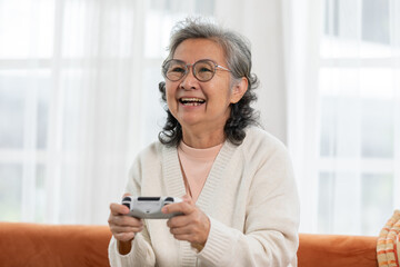 Delighted senior Asian woman immersed in joyful gaming experience at home, showcasing the positive...
