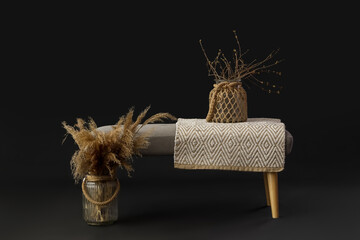 Grey bench with pampas grass and tree branches in vases on black background - obrazy, fototapety, plakaty