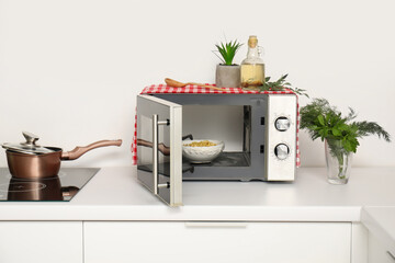 Bowl with pasta in modern microwave oven on white kitchen counter
