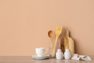 Kitchen utensils, cup and saucers on wooden table near beige wall