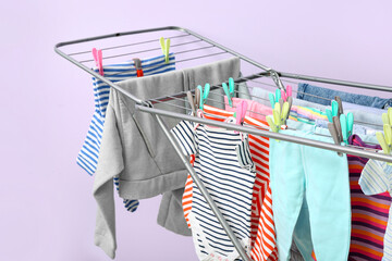 Clean baby clothes hanging on dryer near lilac wall