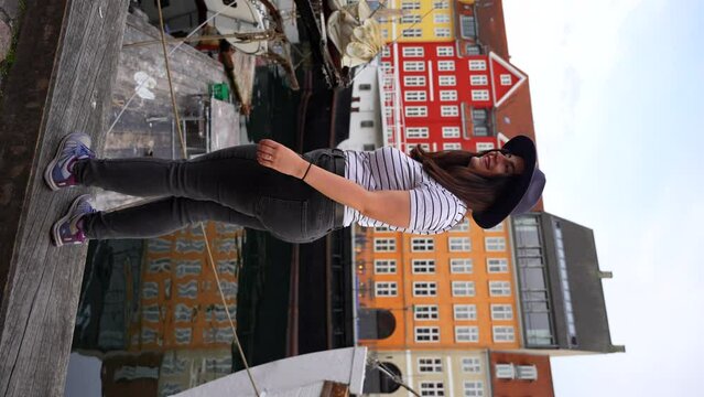 Woman in hat standing by the promenade in Nyhavn turns back smiling at camera in Copenhagen. Vertical