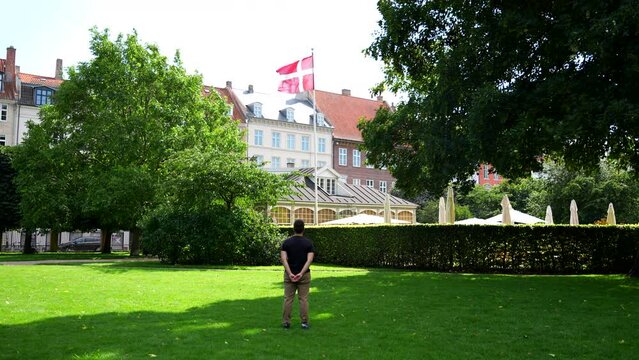 Back view of man looking at Danish flag waving with the wind in Copenhagen, Denmark. Static, slowmo
