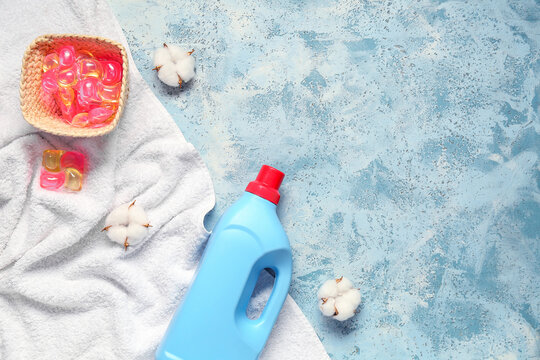 Different laundry detergents, clean towel and cotton flowers on blue grunge background
