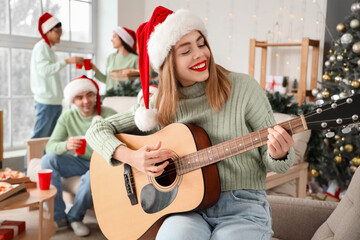 Young woman playing guitar at Christmas party with her friends