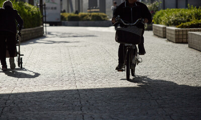 冬の朝の街で自転車を乗っている女性と補助車を押して歩くシニア女性の姿