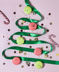 Christmas tree made of green ribbon. Christmas ornament balls, macarons and Christmas canes on pastel background