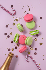 Creative Christmas and New Year composition with golden champagne bottle, confetti, pink and green macarons, Christmas canes, pink background. Flat lay.