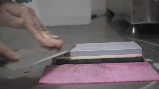Side view close up of cook sharpening a knife using a whetstone 4K
