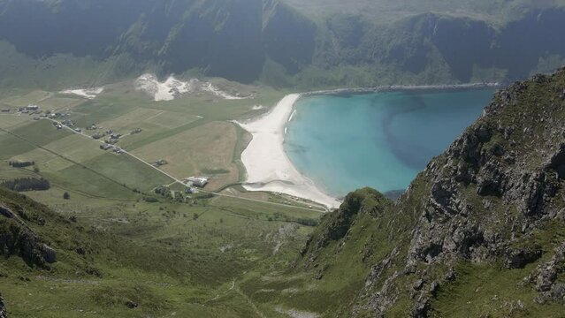 Aerial tilt down shot of green mountains with sandy beach and turquoise bay of Hoddevik in Norway