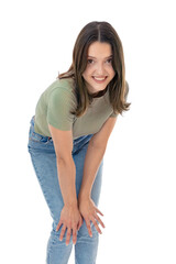 Charming young caucasian woman leaned on her knees, looks with happy expression, solated on white background. Happy brunette girl in green T-shirt and blue jeans smiling and posing in studio.