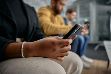 Three multiracial young adults in businesswear sitting and scrolling on mobile phones in office
