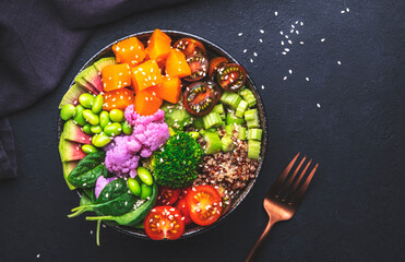 Vegan buddha bowl with pumpkin, quinoa, tomatoes, spinach, celery, radish, soybeans, edamame, tofu, cauliflower, broccoli and seeds, black table background, top view. Autumn or winter healthy food