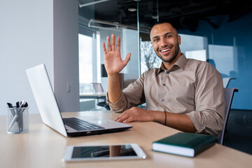 Portrait Satisfied African American businessman in office, working on laptop, tapping on keyboard, greeting waving hand looking at camera.