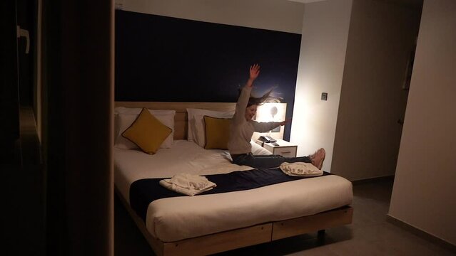 A girl jumps on a hotel bed.