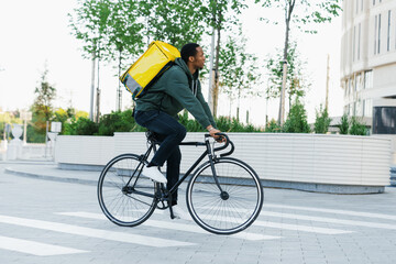 An African-American delivery man with a yellow backpack rides a bicycle. A man is in a hurry to order.