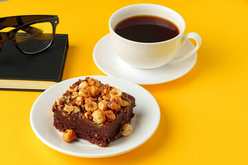 Piece of brownie cake with hazelnuts on yellow background