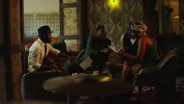 Modern African American jazz band of four sitting around table in vintage style jazz club and working on new song together while rehearsing for concert