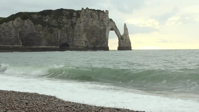 The English Channel waves with cliffs Aval and Needle of Etretat in the background, France