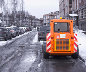 A small orange snowplow removes melted snow from the driveway