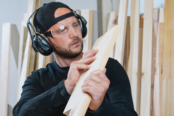 A bearded man inspects the boards before starting to work. Manufacture of furniture products.