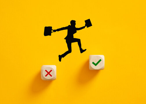 Silhouette of a businessman jumping from wrong cross symbol to right check mark symbol on wooden cubes.